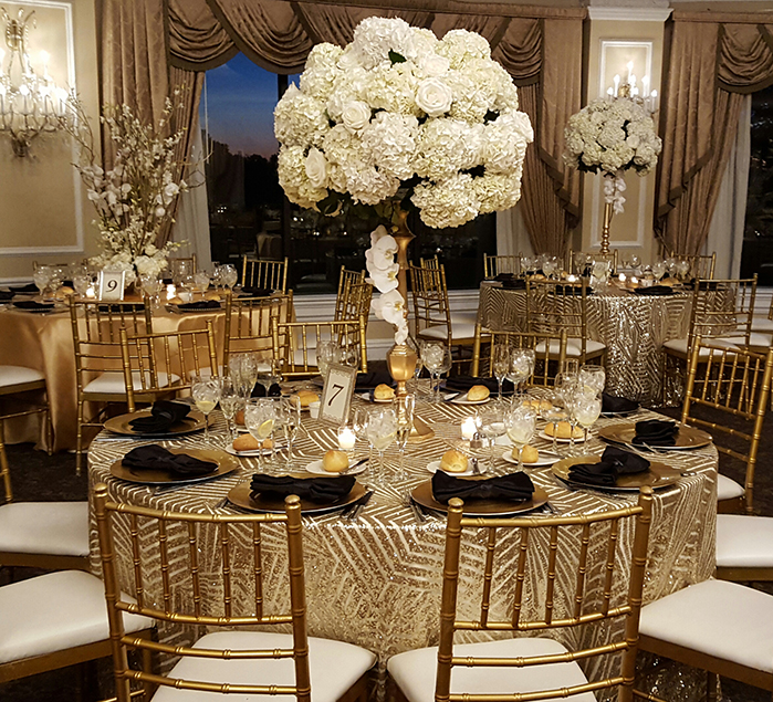 Gold tablecloth with black napkins and white tall centerpiece.